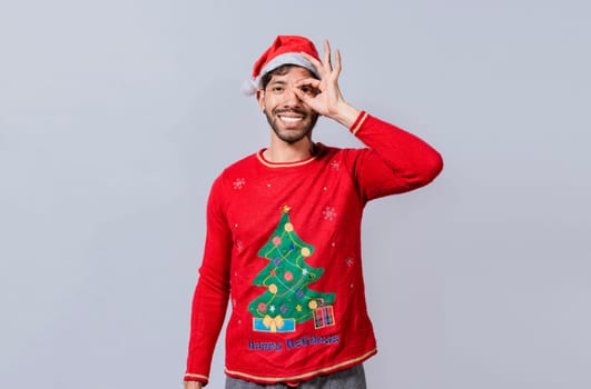 Funny young man in christmas hat looking through fingers. Funny christmas guy making gesture and looking through fingers, Man in christmas hat making gesture looking through fingers