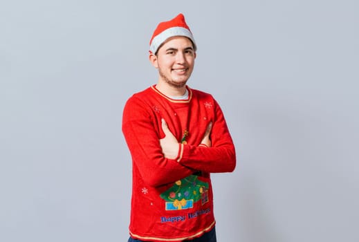 Portrait of guy in sweater and christmas hat with crossed arms isolated. Smiling guy in christmas hat with crossed arms smiling. Teenage guy in christmas clothes with crossed arms smiling