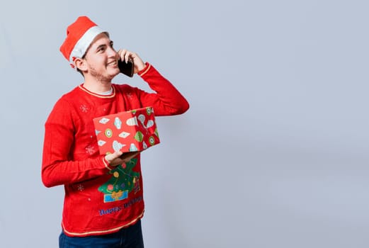 Christmas man holding gift and calling family on phone. Happy man holding gift and calling family at christmas, Smiling guy in christmas hat holding christmas gift box and talking on the phone