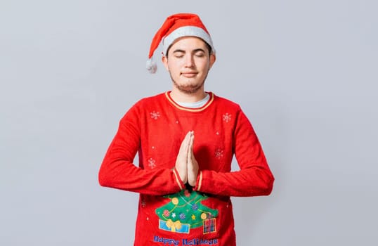 Guy with hands together praying in christmas isolated, concept of person with christmas hat praying and making a wish. Man with christmas hat with praying hands isolated