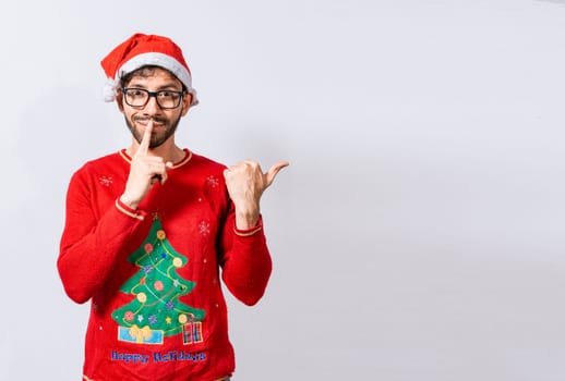 Man in Christmas sweater in silence gesture pointing to the side, Guy in Christmas hat with finger on lips pointing side. Bearded man in christmas hat in silence gesture pointing promo