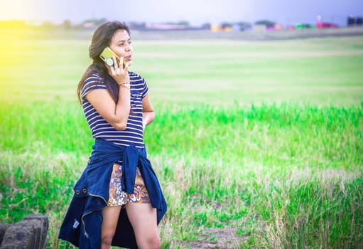 Young girl calling phone on the green field, Beautiful young woman calling by cell phone on the grass outdoor.
