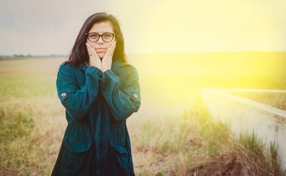 Close up of woman with glasses in the field, Girl in glasses with hands on cheeks