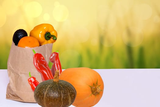 Closeup of a brown paper shopping bag with fresh vegetables and two pumpkins on table over abstract blurred autumn background. Space for food and product display montage. Concept of strengthening the immune system.