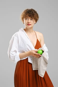 Woman wiping an apple with a towel and looking to the side. Concept of healthy eating and vitamins in ordinary products