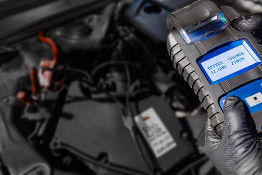 Explore automotive diagnostics as a mechanic holds a battery tester under the hood, displaying Defect and Change on the screen above the car battery, indicating the need for replacement. Ensure optimal vehicle performance with timely battery maintenance.