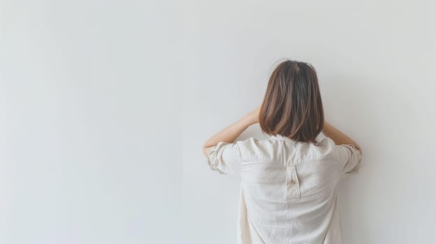 A woman is standing with her back to the camera against a wall. She appears to be still and contemplative in the urban environment.