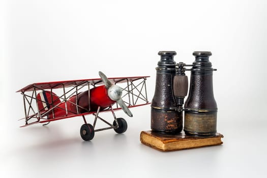 Antiques including film gear, tin aeroplanes, aged binoculars, and diaries on a white canvas, symbolizing age-old quests and revelations