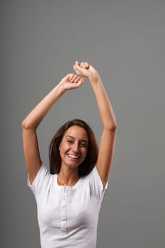 Dance or great joy and frenzy with raised arms. Emotional portrait of a young woman isolated on a neutral background. Long brown hair, slim, white shirt. State of mind concept