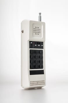 White cordless plastic phone with a metal telescopic antenna, a relic of the 1980s, standing vertically on a white background, anonymous language on black keys. Before the rapid evolution of telecommu