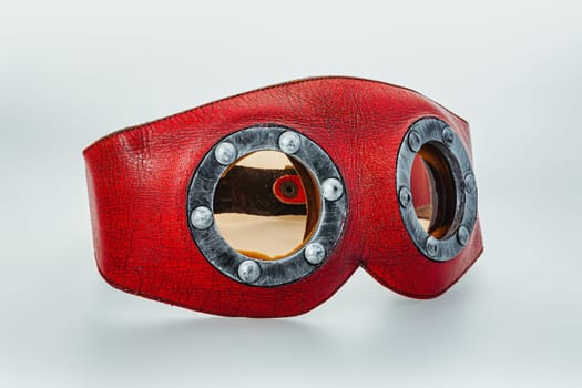 Close-up of a red steampunk leather mask with riveted round goggles on a white background. Ideal for superheroes, pilots, or eccentric characters in search of unique items