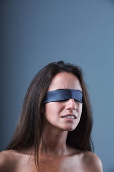 Blindfolded young woman with an expression of mild fear or discomfort, as if from noise or pain. Suffering, fear of the unknown, hidden dangers and information. Bare shoulders convey vulnerability