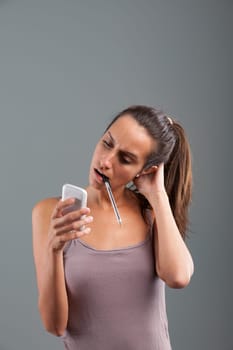 'What do I do now?' thinks the girl after receiving news on her phone, nervously holding a pen in her mouth, touching her nape. Emotional portrait, brown hair, slim, beige tank top. State of mind conc