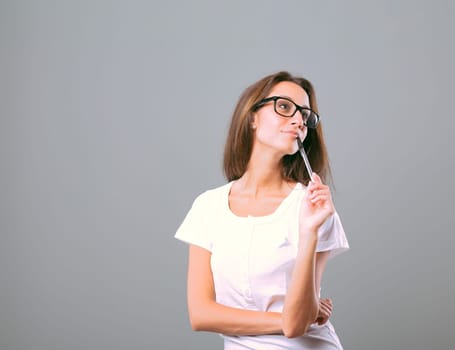 Portrait of a young woman experiencing an emotion or sensation, thinking about something fascinating or pleasant, holding a pen in her mouth, wearing glasses and a white shirt, beautiful and slim