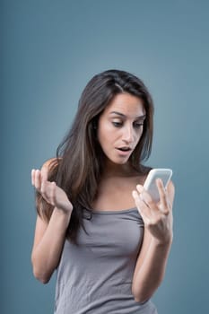 Emotional portrait of a young woman isolated on a neutral background. Surprised on the phone. Girl in a shocking moment due to something on her cellphone, with a bewildered hand gesture. Long brown ha