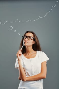 State of mind portrait of a young woman isolated on a neutral background. Thoughtful girl looks up, imagining, inventing. Arms crossed, pen to mouth with one hand. Perhaps a revolutionary idea. Long b