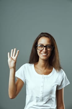 Young woman, glasses, white shirt, frontal portrait, raising hand, four fingers up, forming number four or representing a quarter fraction. Part of one-to-five series