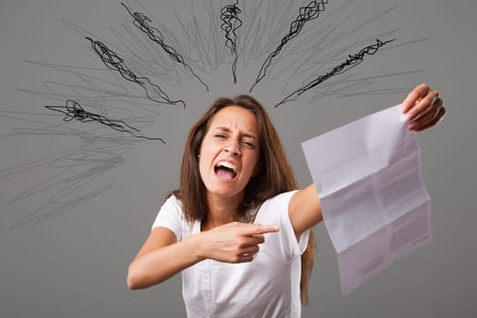Emotional portrait of a young woman isolated on a neutral background. She points to a letter she's holding, her face showing anger and frustration, a negative reaction to the injustice and problems co