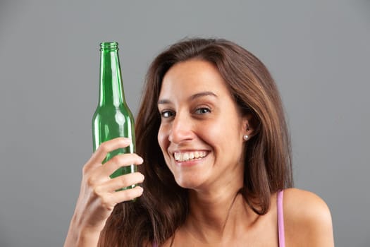 Funny expression in close-up portrait of attractive young woman holding green beer bottle - concept of glass recycling