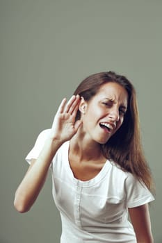 'What did you say? I can't hear you!' seems to be the meaning behind young woman's hand to ear gesture and annoyed expression. Beautiful, slim, long-haired, possibly sarcastic