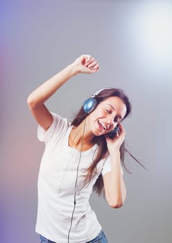 Girl wearing blue headphones listens to music, dancing and singing, surrounded by sparkling, frantic party lights. Joy, happiness, and fun from music visible on slim, long-haired young woman's face