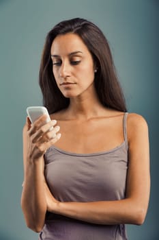 Young woman looks at her cell phone screen, serious and upset. About to get angry or just containing and holding back her furious wrath. Bad news or incoming annoyances and issues. Maybe the phone is