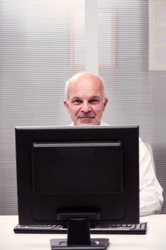 Amidst the confines of a tight office space, a peaceful smile graces the face of a senior businessman, peeking from behind his computer screen