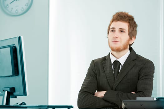Young clerk in an office looks up thinking or dreaming. Is he planning for the future of the company or fantasizing about his upcoming beach vacation? Wide copyspace.