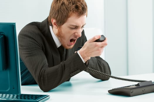 Controlling aggression in the work environment may be necessary. Man in a suit in the office yells violently at the telephone by grabbing the handset firmly and pouring all his anger into it by shouti