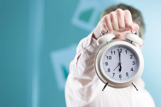 Against a blurry office backdrop, a hand extends a sizable clock. In the corporate world, time is invaluable, and deadlines are near. Stay nimble!