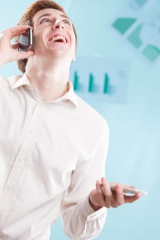 A boisterous man in office attire, laughing while on a smartphone call. His rosy hair and the bluish business backdrop suggest he's received good news from abroad