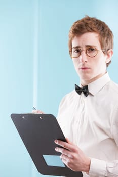 A young man in an old-fashioned office suit, possibly a nerdy, slightly servile accountant, grips a notepad. His sad gaze, white shirt, and bowtie stand against a blurry office setting
