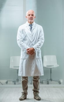 devoted healthcare worker in white coat stands with determination. Balding, middle-aged, he keeps fit for service. Underneath, a shirt and tie hint at his seriousness