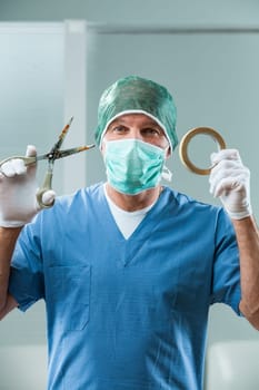 Surgeon in an operating room uses rusty scissors and paper tape. His ironic smile reveals the urgency for strict hospital tool regulation