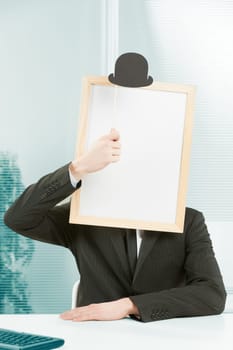 Man with framed sign head in an office. On top of the fake head made of signboard he also puts a bowler hat for a strange and funny but also elegant look.