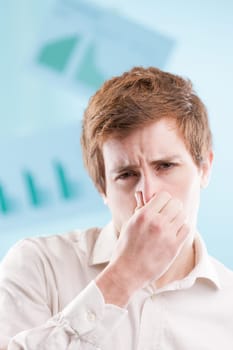 Young man with red hair, clad in a white office shirt, pinches his nose in displeasure. With a blue business backdrop, he's tolerating unsavory practices just to keep working