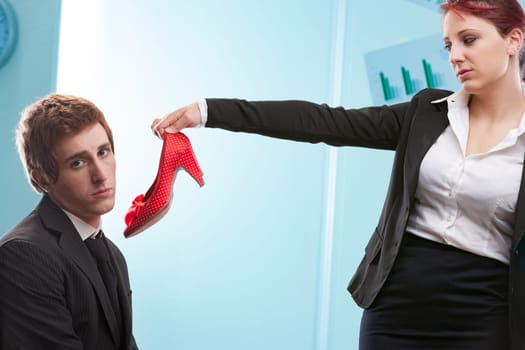 Man offered heels by woman: her stand against fashion serving male tastes. Turning tables on traditional dominance, she reflects past actions