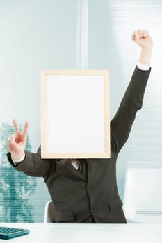 Businessman with sign head has one hand raised in jubilation and with the other forms a victory sign. A computer keyboard can be glimpsed on the desk. There is great enthusiasm at the workplace for th