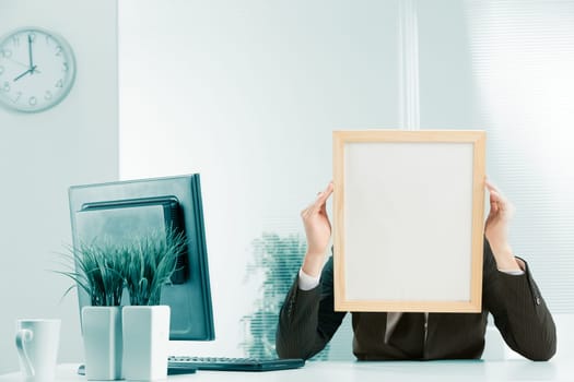 Office workplace, a sign-headed man framed in light wood holds the sign-head with his hands. Either he is very worried or he is pressing his temples with a headache. A PC monitor is visible on the des