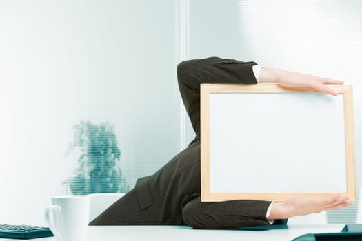 Office workplace, a sign-headed man framed in light-colored wood leans to the side from a fainting spell, a shock from strong negative news. He holds up the sign-head perhaps also from a headache.