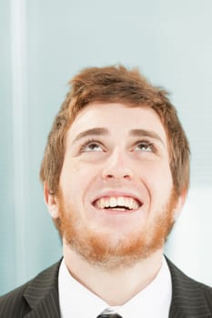 Close-up portrait of young man with short red hair and beard. Joyful and somewhat foolish expression as he looks up smiling or laughing happily, chin raised, vertically to the axis.