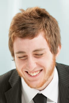 Close-up portrait of young man with short red hair and beard. Positive expression of laughter, his eyes are closed and he is trying not to laugh but he can't help himself and is snickering happily.