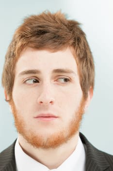 Close-up frontal portrait of young man with short red hair and beard. Suspicious expression, feeling of risk: something is approaching to his right and he is getting worried.