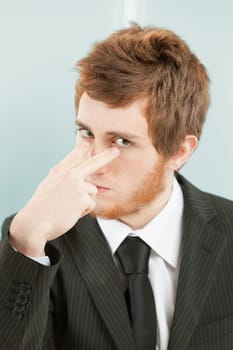Close-up portrait of young man with short red hair and beard in suit and tie. He points to his own eyes with index and middle fingers, as if to say that he is watching you, controlling you, and you ca