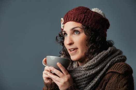 Embraced by winter, a woman in woolen attire sips a comforting drink like milk, café latte, or chocolate. Settled in a mountain retreat or café, she gears up for errands with her vivid eyes gleaming
