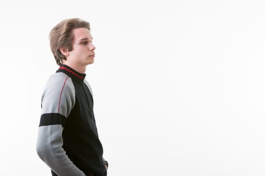 young man in a black, gray, and red-striped sweater stands with hands in pockets, gazing toward the COPYSPACE on the right. With a slightly sporty, wintry look, his light brown hair is short, and he w