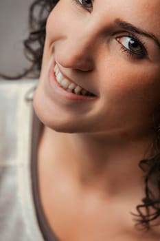 Portrait of a young woman with curls. The future, in her eyes, holds potential. She smiles, revealing healthy teeth, uninterested in diet fads. Her vibrant eyes hint at the momentary illusion of bound