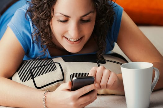 curly-haired lady lies comfortably on floor cushions at home, deeply engrossed in her phone's multifaceted world. Social media, video games, streaming, adult content, and dating apps are all at her fi