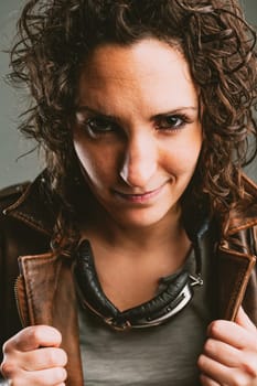 Frontal portrait of a female biker in leather jacket and goggles. She has a defiant look and poses as a boss. Tough lady this one!
