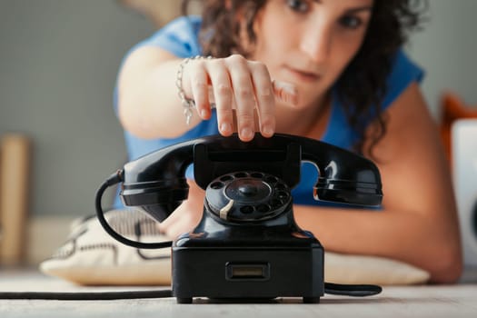 prominent black vintage rotary phone in focus epitomizes the direct nature of voice calls. Lift the receiver, speak to another human. Behind, a blurred young woman reaches for the handset. It symboliz
